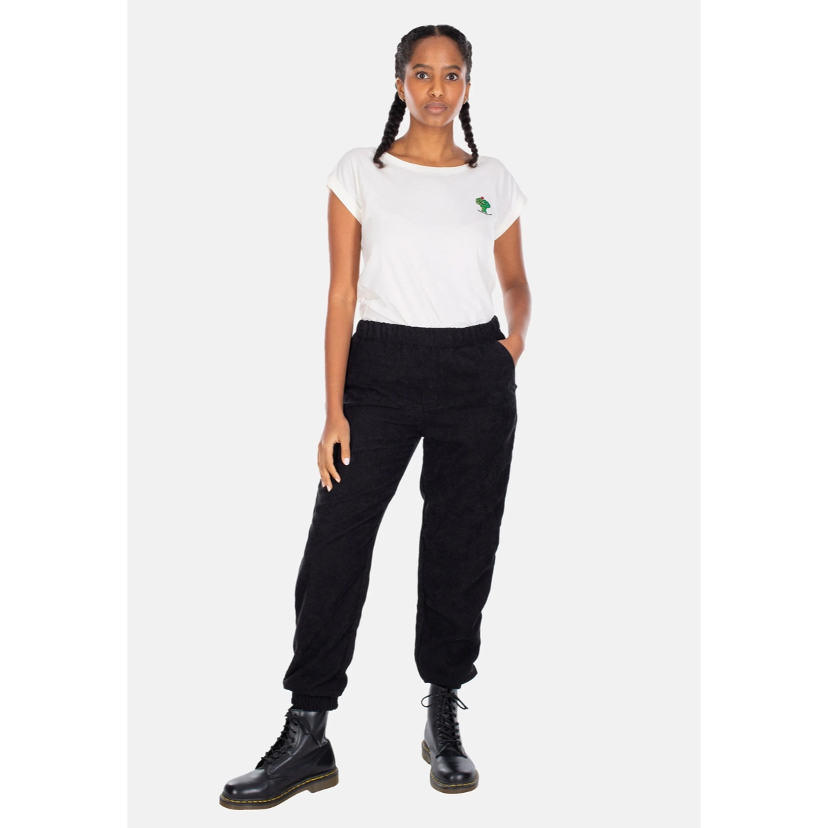T-shirt blanc à manches courtes avec logo vert, pantalon noir, bottes, style décontracté