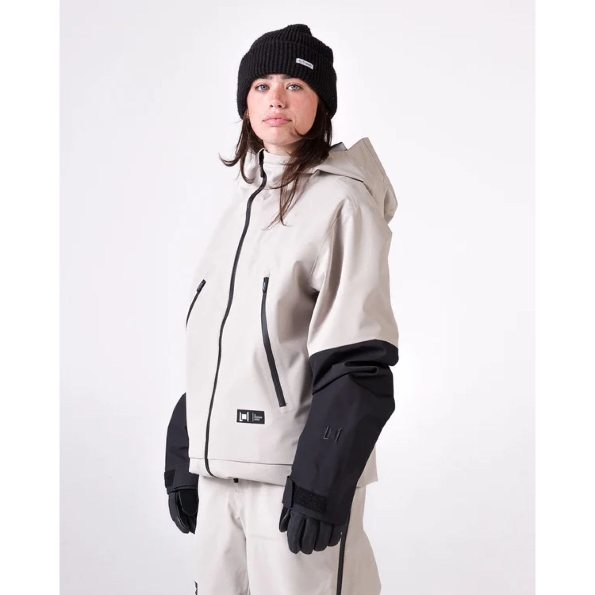 Veste de neige, manteau beige, capuche, poches zippées, manches noires, veste de ski, combinaison de ski, fermeture éclair, capuche, contrastes de couleurs beige-noir