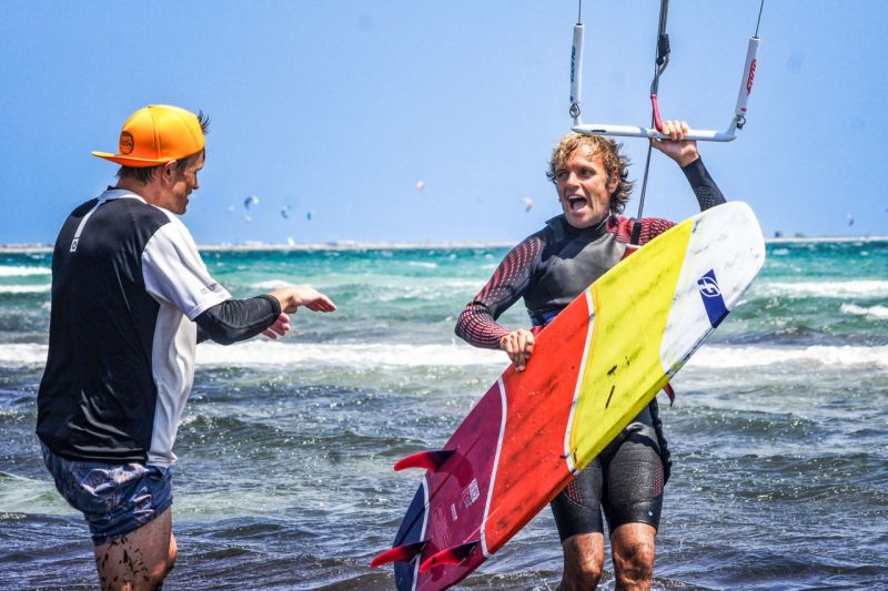 Des moniteurs de kitesurf et des kitesurfeurs avec leur planche rient dans l'eau au Kitecamp