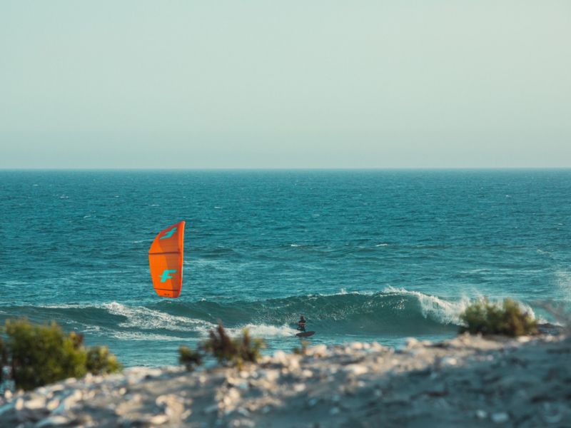 Cerf-volant orange au-dessus d'une vague, vue depuis la côte